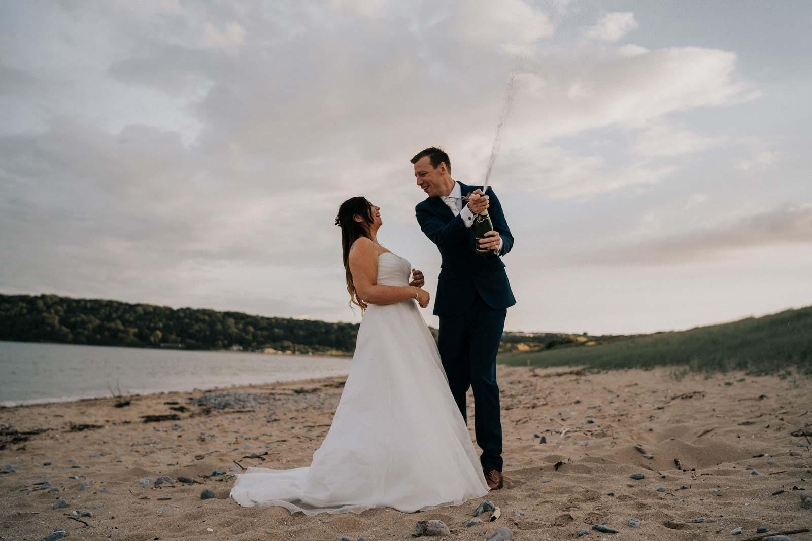 bride and groom pops a bottle on the beach