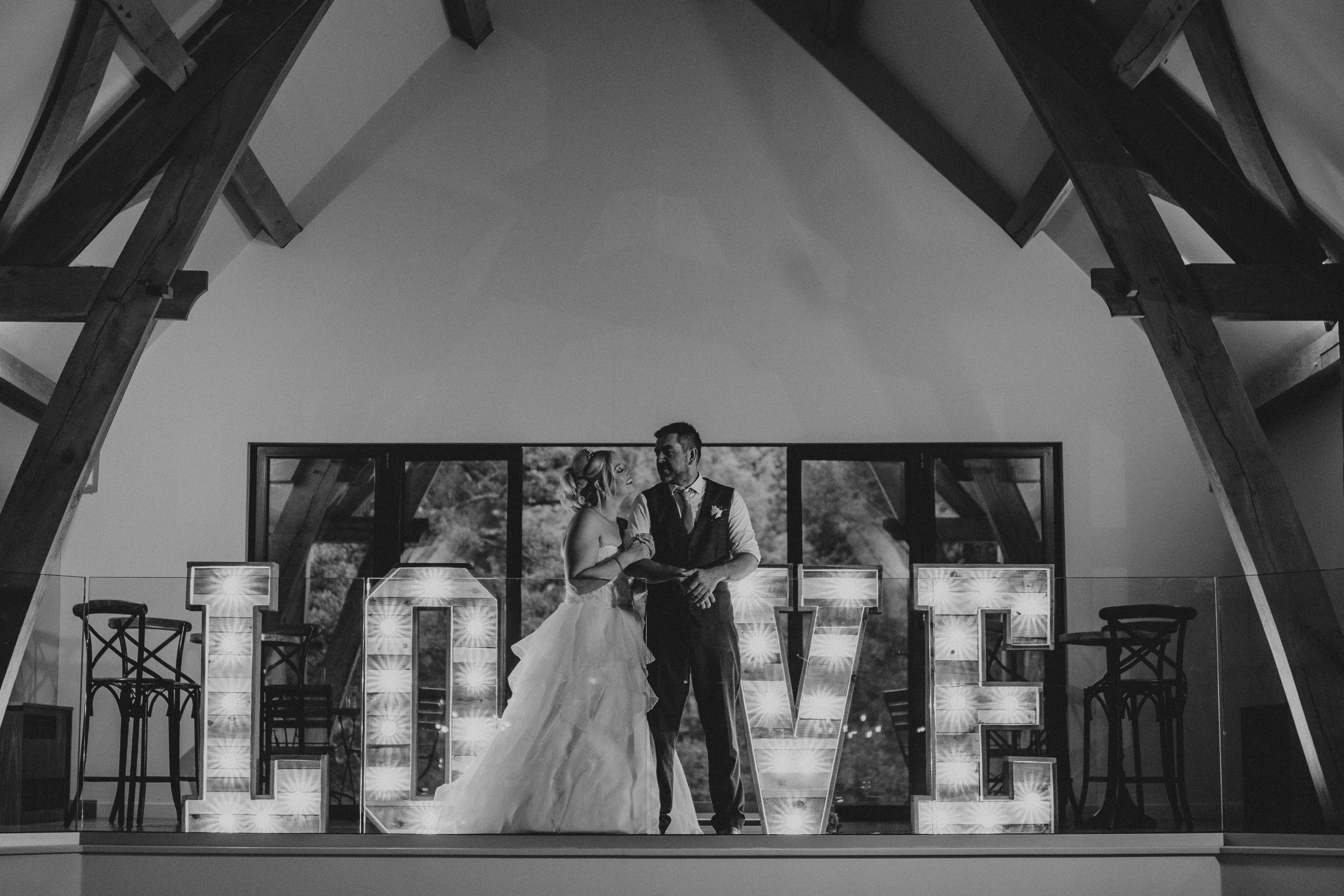 Bride and groom stand in front letters which spell out love - The Mill Barns