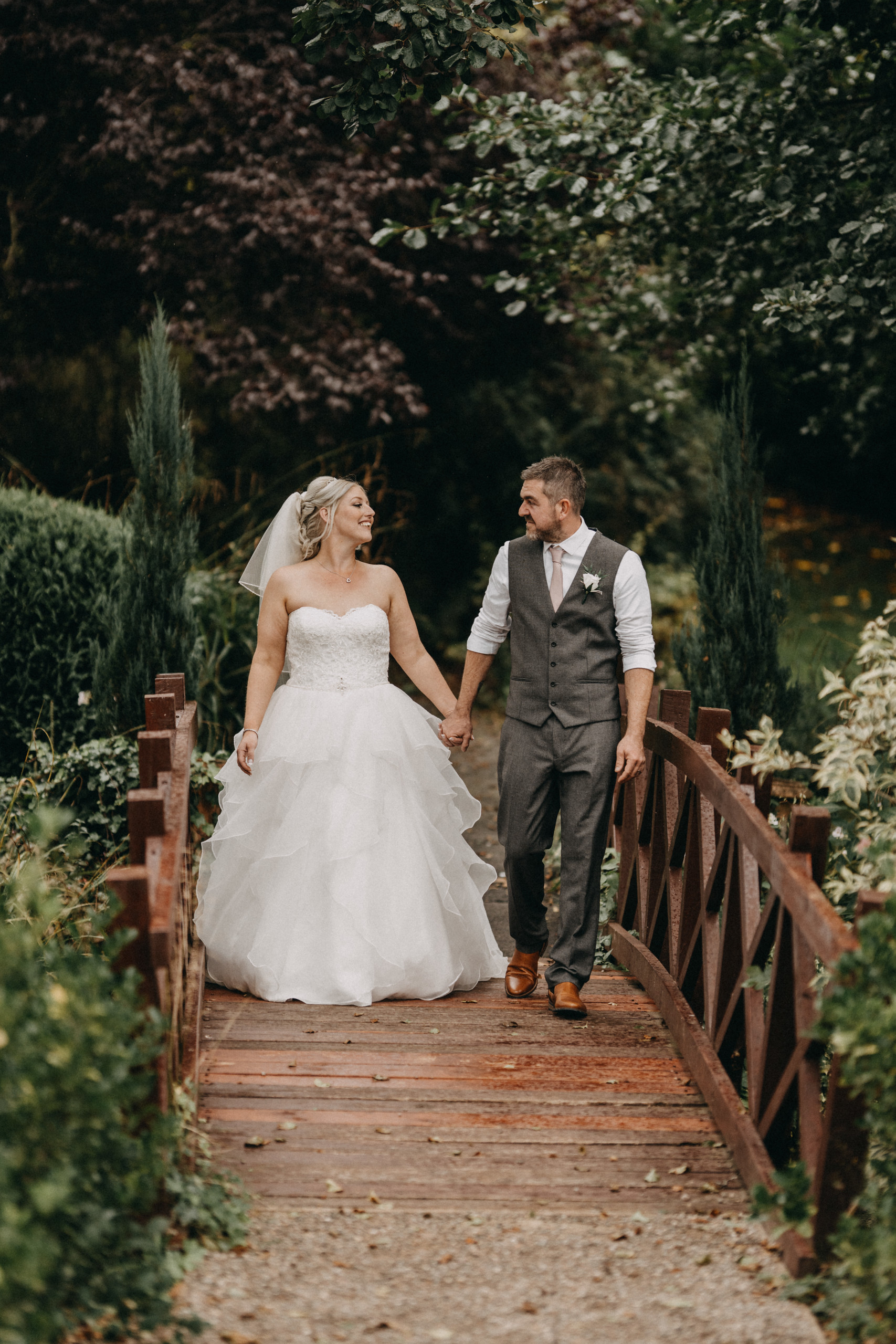 Bride and groom walk across a bridge, in the setting outside - The Mill Barns