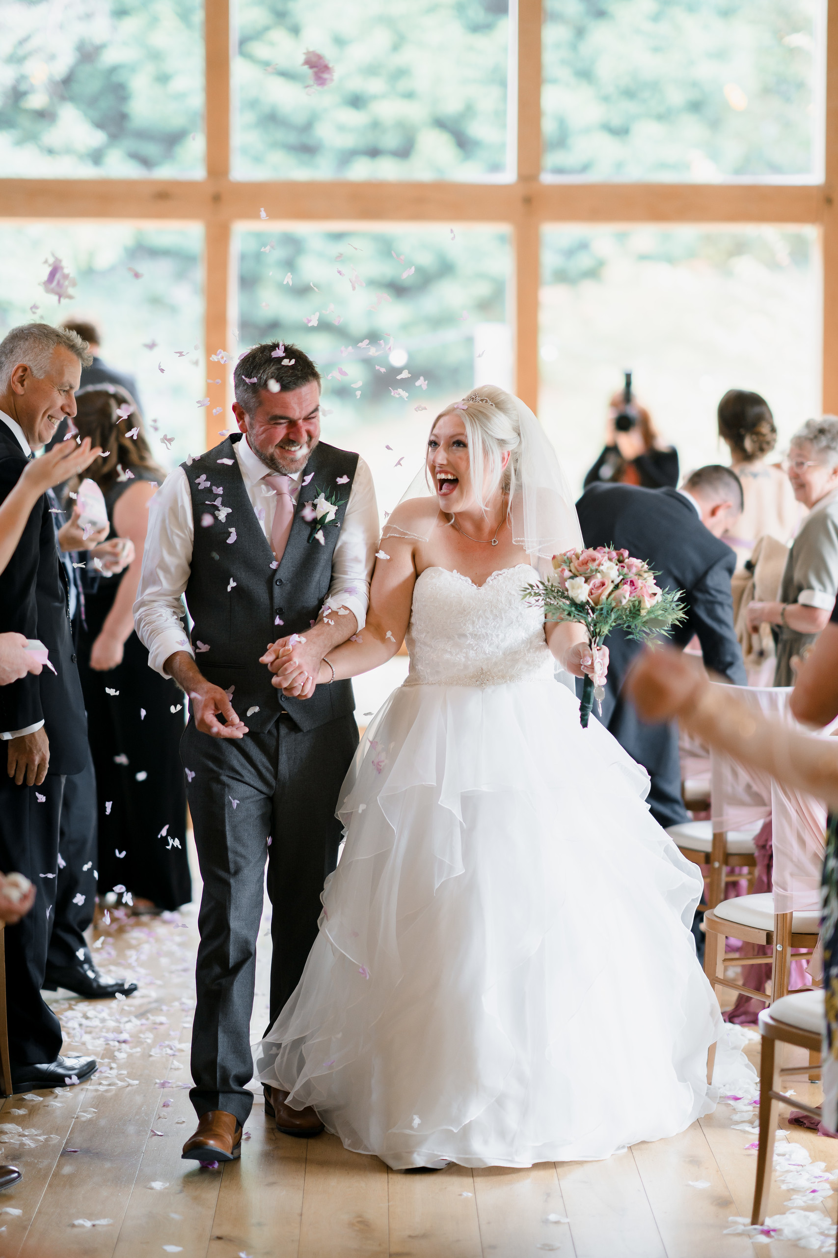 Bride and groom walk back up the aisle together as family and friends throw confetti