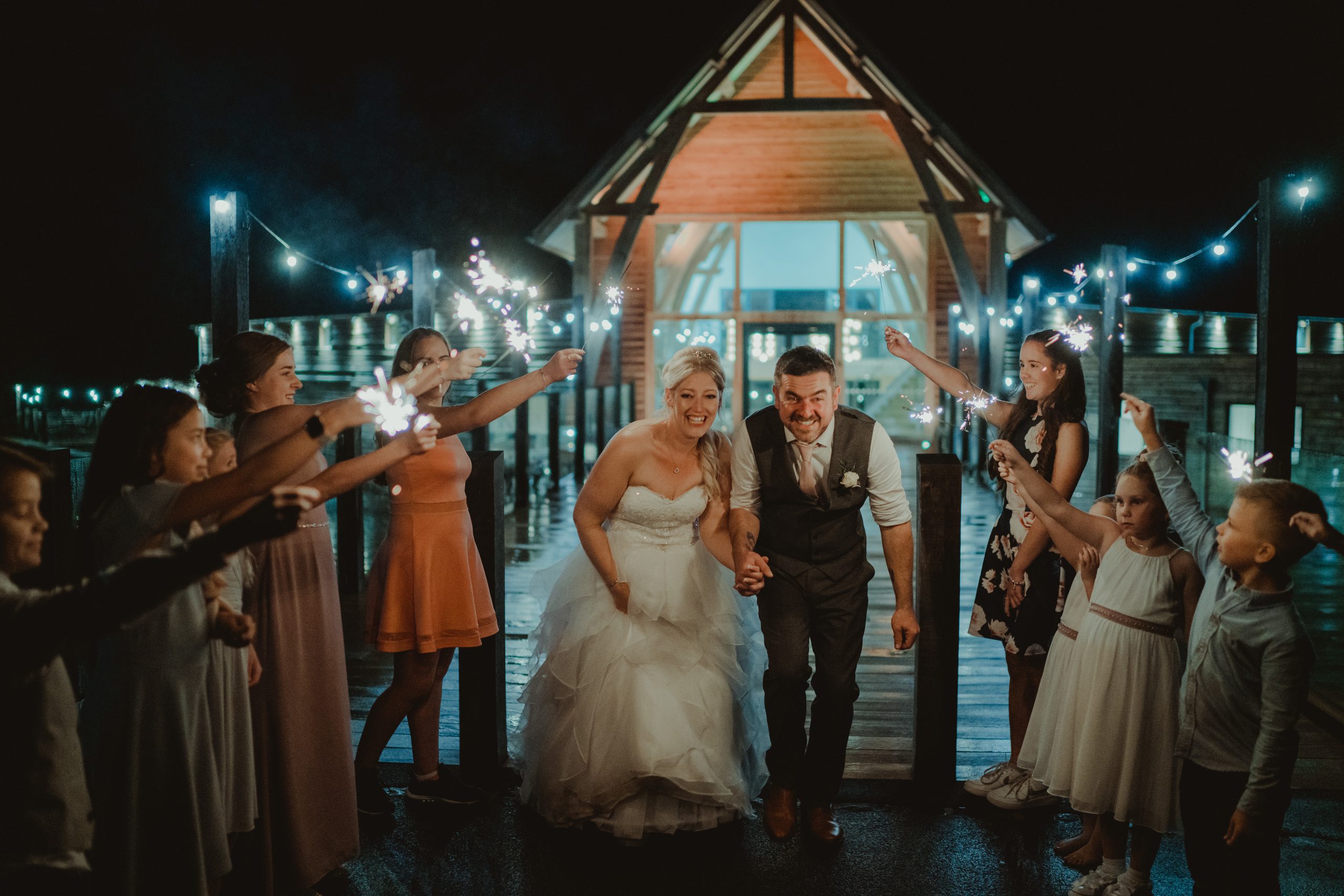 Bride and groom walk through sparklers held by family and friends - The Mill Barns