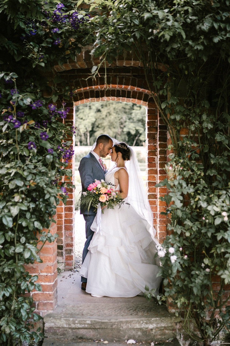 Bride and groom Hold each other close under a archway in their wedding venue| Wedding Photo