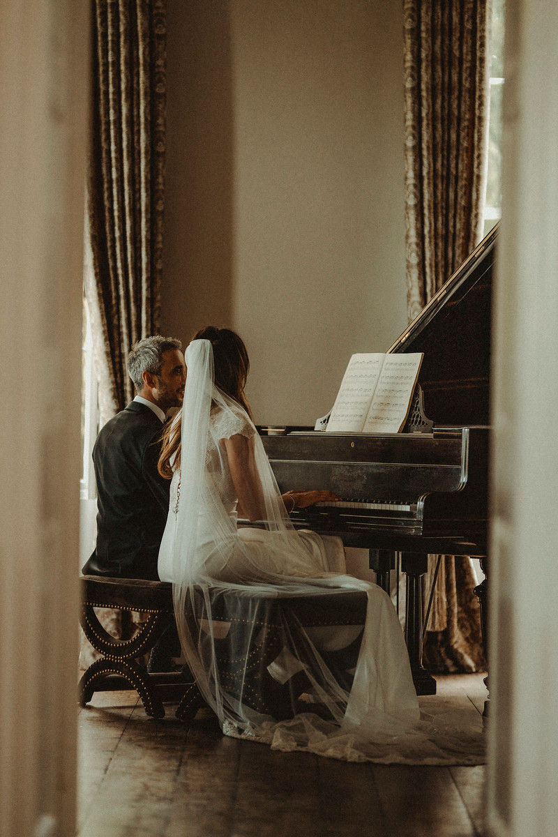Bride and groom sat by a grand piano. Wedding pictures