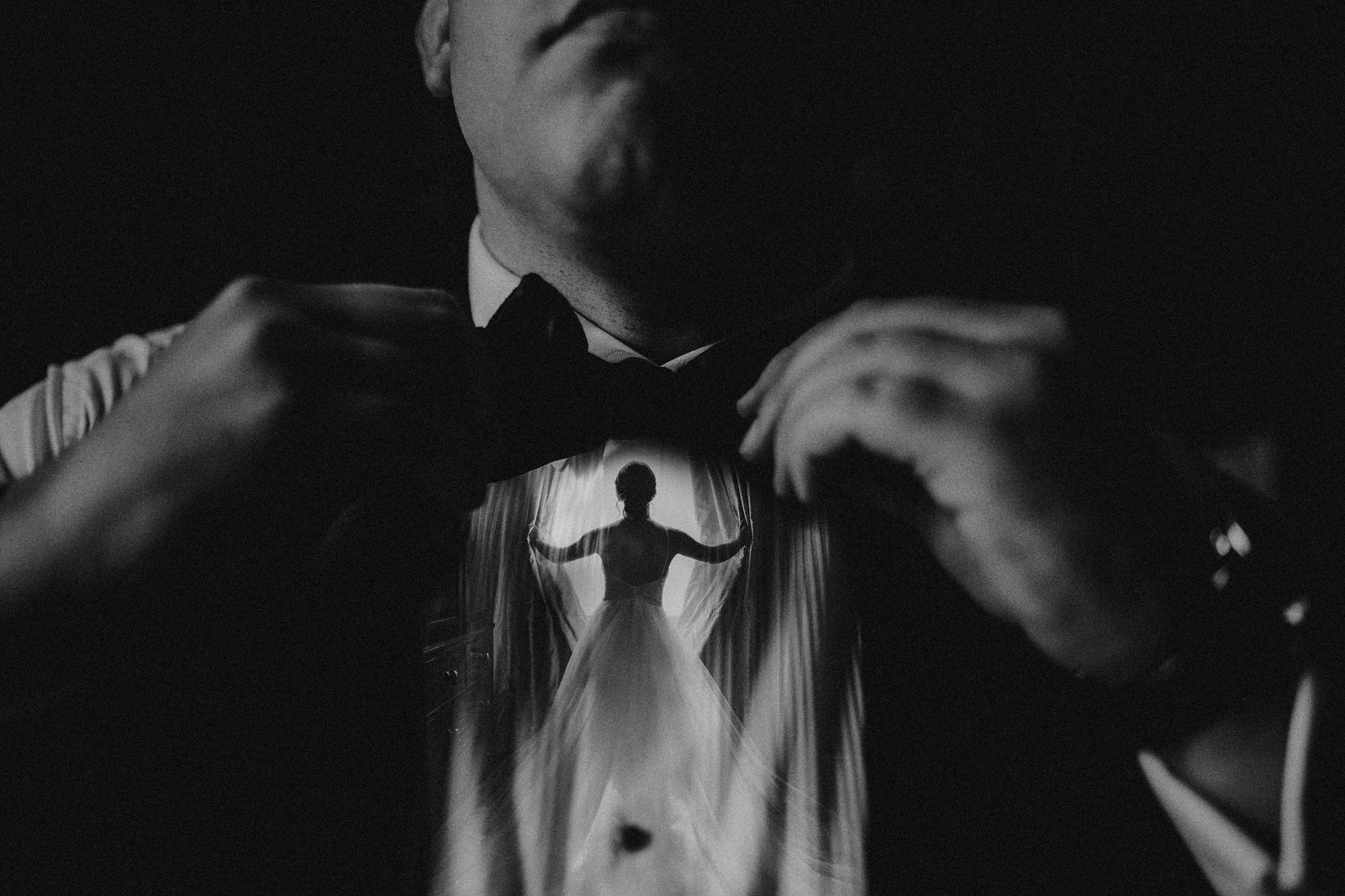 a reflection of the bride opening curtains is reflected in the grooms shirt